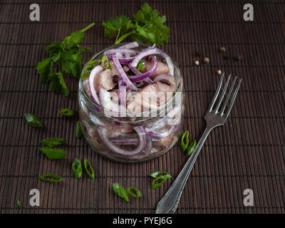 Le filet de hareng salé, coupé en morceaux et parsemé de boudins d'oignon rouge, se trouve dans un bocal de verre Banque D'Images