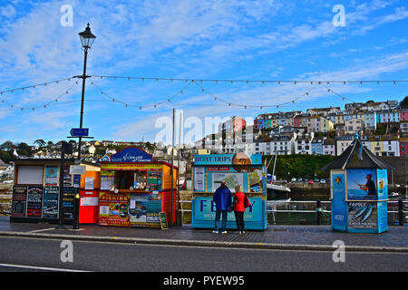 Un couple toutes les petits kiosques qui tapissent l'harbourside à Brixham vente de voiles de bateau et des voyages de pêche pour les résidents et les touristes. Devon, Angleterre, Royaume-Uni Banque D'Images