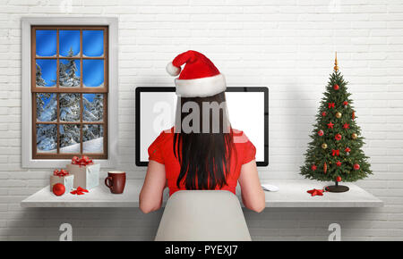 Fille travailler sur ordinateur durant les vacances de Noël dans son bureau entouré de décorations de Noël. Vue depuis l'arrière. Banque D'Images