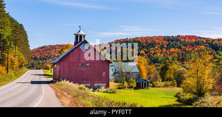 Route de campagne avec grange rouge le long d'une route rurale de pays avec des bois habillés dans des couleurs d'automne de l'automne feuillage Banque D'Images