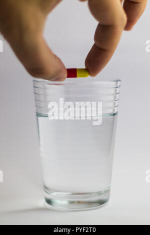 Les hommes donne un comprimé de couleur rouge et jaune dans un verre d'eau, de la médecine Banque D'Images