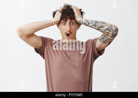 Le temps jouant contre guy. Choqués et inquiets concernés beau jeune homme avec moustache et curly hairstyle tenant les mains sur la tête laissant tomber jaw étant en difficulté et situation perplexe Banque D'Images