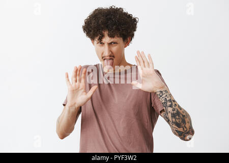 Garder cette chose loin de moi. L'homme tatoué élégante exprimant le dégoût et l'aversion de palmiers pour se protéger de la nourriture qu'il déteste sticking out tongue et froncer de déplut à émotions Banque D'Images