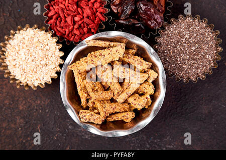 Divers de l'air dans un petit bol près de muesli sur fond noir. Superfood comme chia, fève de cacao brut, le goji, le gruau. Copier l'espace. Mise à plat. Banque D'Images