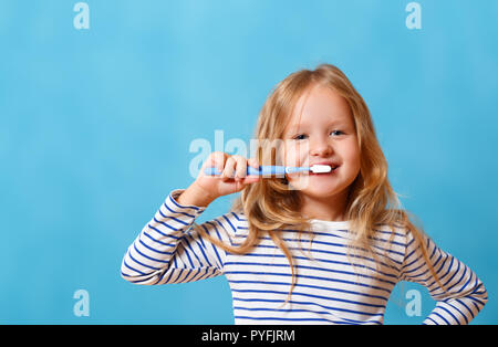 Une petite fille en pyjama rayé est se brosser les dents avec une brosse à dents. Le concept de l'hygiène quotidienne. Isolé sur un fond bleu Banque D'Images