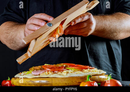 Male chef d'ajouter des tranches de tomate sur pizza non cuite sur table Banque D'Images