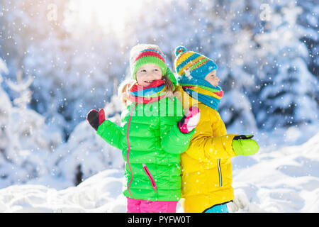 Enfants jouant avec la neige en hiver. Petite fille et garçon en veste colorée et tricoté hat attraper des flocons de neige en hiver Parc sur Noël. Kids jum Banque D'Images