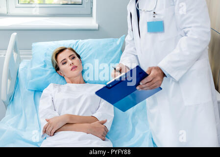 Vue partielle de l'homme médecin avec stéthoscope sur cou pointant vers le presse-papiers pour female patient in hospital room Banque D'Images