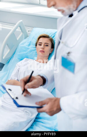 Vue partielle de l'homme médecin avec stéthoscope sur cou écrit dans le presse-papiers près de hot female patient in hospital room Banque D'Images