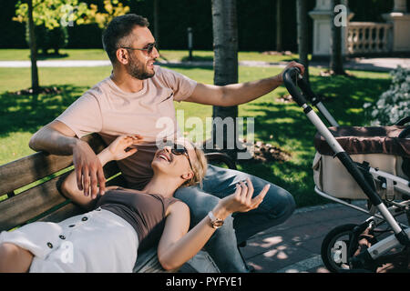 Femme couchée sur mari jambes près de baby carriage in park Banque D'Images