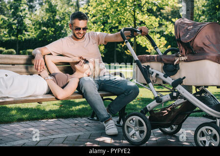 Femme couchée sur mari jambes près de baby carriage in park Banque D'Images