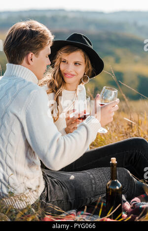 Jeune couple de trinquer avec des verres de vin rouge et relaxant on meadow Banque D'Images