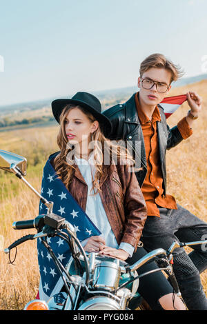 Jeune couple avec drapeau américain assis sur moto, concept de la journée de l'indépendance Banque D'Images