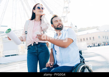 Bel Ami en fauteuil roulant montrant smartphone pour petite amie avec carte sur street Banque D'Images