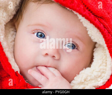 Une petite fille aux yeux bleus dans un rouge chaleureux hood. Banque D'Images