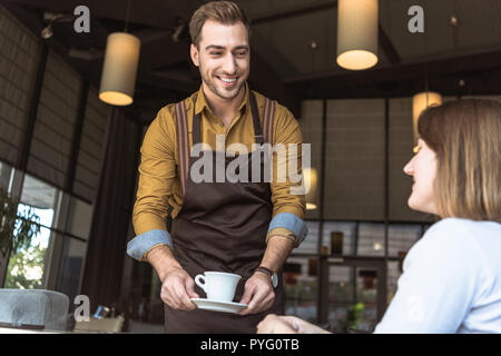 Happy young waiter serving tasse de café pour cliente au café Banque D'Images