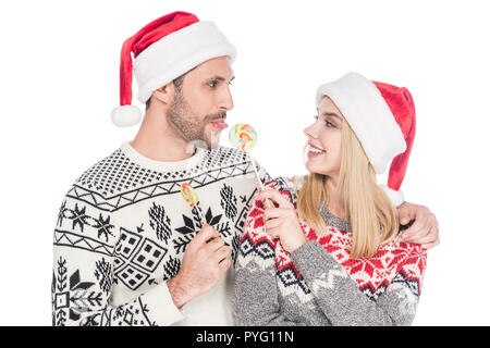 Portrait of young caucasian couple in santa claus hats avec lollipops isolated on white Banque D'Images