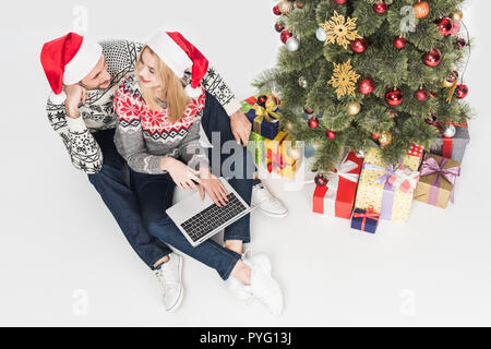 Vue de dessus de couple à santa claus hats with laptop near Christmas Tree isolated on white Banque D'Images