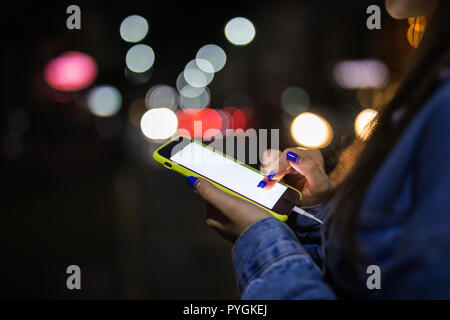 Girl pointing finger à l'écran téléphone intelligent sur l'arrière-plan flou de la lumière dans l'atmosphère de nuit, ville Banque D'Images