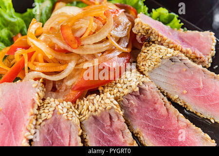 Close Up Portrait of Steaks de thon rôti en croûte de fines herbes et graines de sésame sur la surface gris foncé Banque D'Images