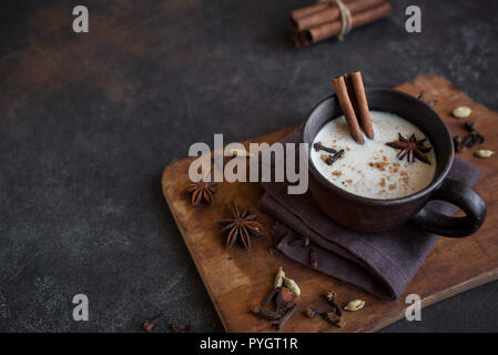Masala chai indien traditionnel plateau en tasse en céramique avec des ingrédients. Thé noir épicé avec du lait sur fond sombre rustique, Close up. Banque D'Images