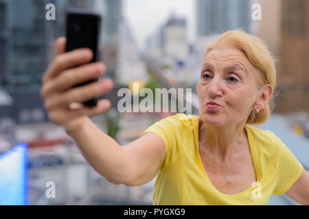 Beaux selfies senior woman taking with mobile phone in city Banque D'Images