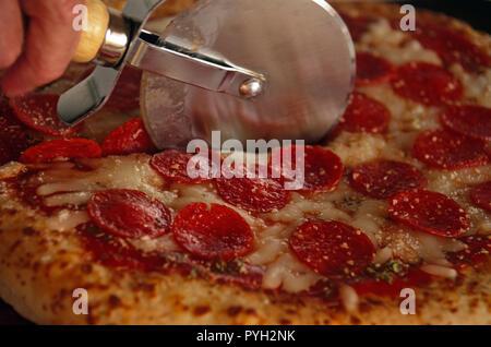 Close up de roue de coupe en tranches une pizza au pepperoni Banque D'Images
