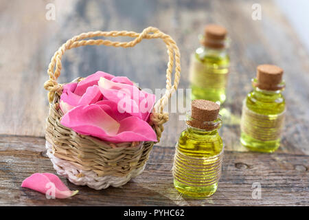 Panier en osier rustique avec des fleurs rose hip rose et des bouteilles d'huile de roses sur fond de bois Banque D'Images