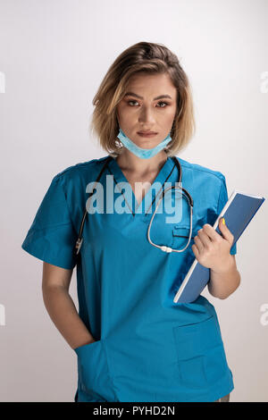 Portrait of young doctor with stethoscope holding paper résultats et posture droite avec main droite dans sa poche. Practicttioner santé special Banque D'Images