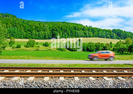 Une voiture se déplaçant rapidement le long de la route passant le long de la voie ferrée. Les voies d'exécution à côté de la route. Une vue ensoleillée d'une voiture passant à travers le pays Banque D'Images