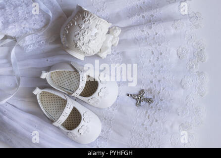 Chaussures bébé baptême, baptême tasse et crystal pendentif Croix sur vintage robe de baptême en dentelle sur fond blanc Banque D'Images