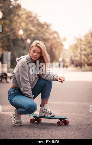 Jeune femme en jeans assis sur la planche à roulettes en parc. Style de vie. Les poils de vol Banque D'Images