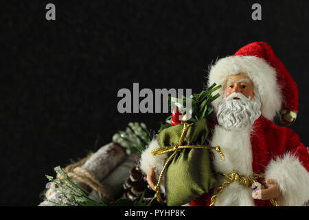 Santa Claus holding un sac de cadeaux close up debout à côté d'attachés ensemble de journaux sur un fond noir avec l'espace d'écriture Banque D'Images