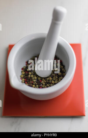 Mortier coloré blanc avec du poivre à l'intérieur sur une tuile rouge sur une table en marbre, cuisine Banque D'Images