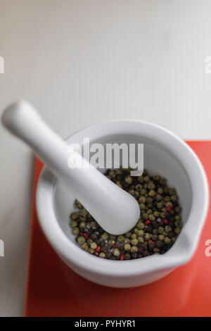 Mortier coloré blanc avec du poivre à l'intérieur sur une tuile rouge sur une table en marbre, cuisine Banque D'Images