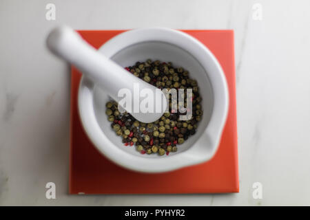 Mortier coloré blanc avec du poivre à l'intérieur sur une tuile rouge sur une table en marbre, cuisine Banque D'Images