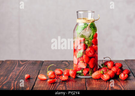 Bouteille de l'eau infusée avec des fraises fraîches et de feuilles de basilic.éparpillés sur les baies de table en bois. Banque D'Images