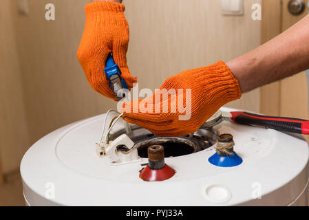 Mains de maître dans la fixation des gants orange ancienne chaudière Banque D'Images