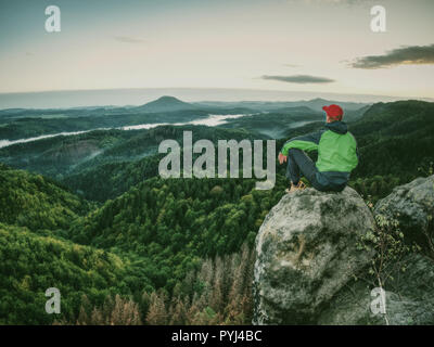 Hiker homme prendre un repos sur le pic. Veste Coupe-vent vert avec Voyageur repose au sol et admire les sommets Banque D'Images