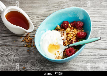 Granola fait maison dans un bol avec les framboises et le sirop d'érable sur une table en bois. Banque D'Images