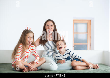 Heureuse mère et deux enfants montrant leurs langues s'assis sur un canapé à l'intérieur de jouer Banque D'Images