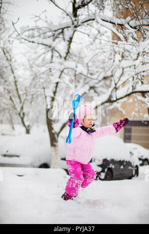 L'enfant joue avec la neige en hiver. Une petite fille dans une gaine lumineuse et tricoté hat, les captures des flocons de neige dans un parc d'hiver pour Noël. Banque D'Images