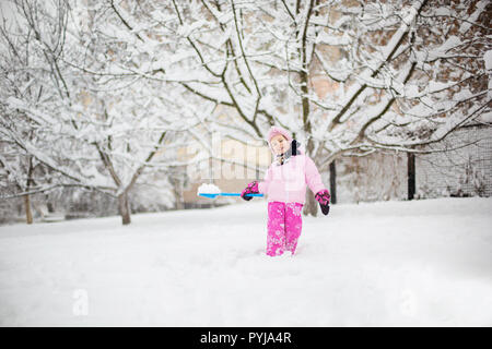 L'enfant joue avec la neige en hiver. Une petite fille dans une gaine lumineuse et tricoté hat, les captures des flocons de neige dans un parc d'hiver pour Noël. Banque D'Images