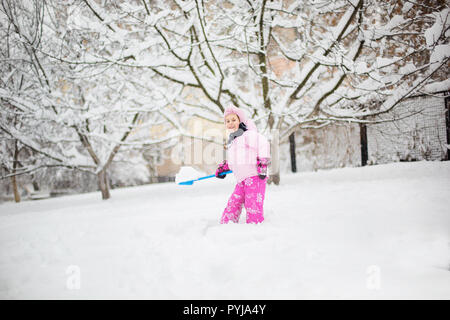 L'enfant joue avec la neige en hiver. Une petite fille dans une gaine lumineuse et tricoté hat, les captures des flocons de neige dans un parc d'hiver pour Noël. Banque D'Images