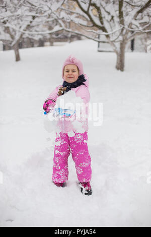 L'enfant joue avec la neige en hiver. Une petite fille dans une gaine lumineuse et tricoté hat, les captures des flocons de neige dans un parc d'hiver pour Noël. Banque D'Images