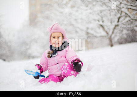 L'enfant joue avec la neige en hiver. Une petite fille dans une gaine lumineuse et tricoté hat, les captures des flocons de neige dans un parc d'hiver pour Noël. Banque D'Images