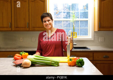 Une femme tient un couteau dans sa belle cuisine maison prête à trancher les légumes Banque D'Images