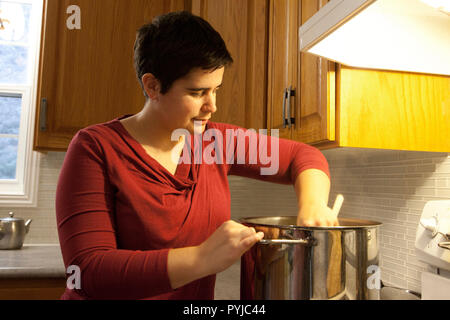 Femme utilise une cuillère en bois pour incorporer un énorme chaudron dans sa cuisine Banque D'Images