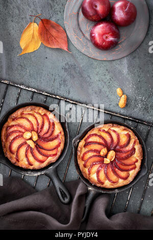 Plum crumble maison tartelettes cuites dans de petits poêlons en fer sur grille de refroidissement. Déposer sur le dessus des tartelettes sur fond texturé gris foncé avec un peu de pruneau, de noix Banque D'Images