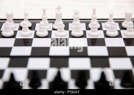 Petite poche échecs, pièces d'échecs en plastique placés sur un échiquier sur un fond de bois blanc Banque D'Images